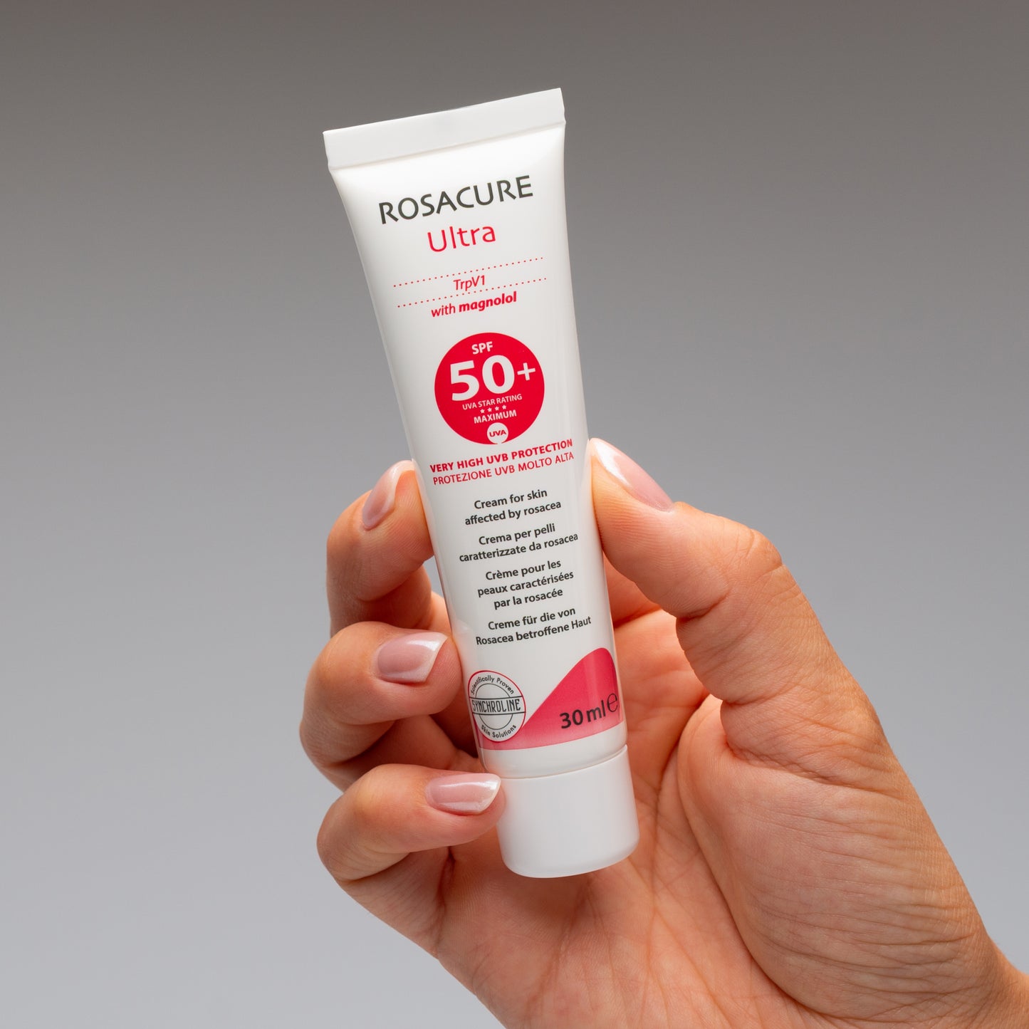 Hand holding a Rosacure Ultra SPF 50+ tube for Skin Affected by Rosacea against a gray background